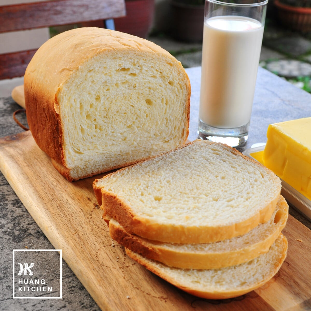 Basic White Bread Bread Machine Recipe by Huang Kitchen - Close Up of loaf slices on wooden board with milk and butter
