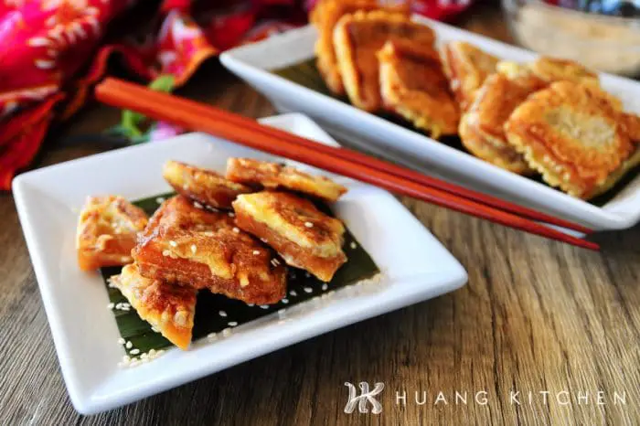 Pan Fried Nian Gao Recipe by Huang Kitchen - Cross section of sliced fritters with gooey inside arranged on a plate, with chopstick and fritters in the background