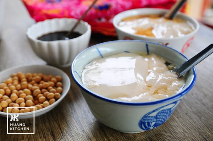 Tau Foo Fah Recipe (Douhua / Soybean Pudding) Recipe by Huang Kitchen - top down with ginger syrup, in blue porcelain bowl with soybeans and batik background